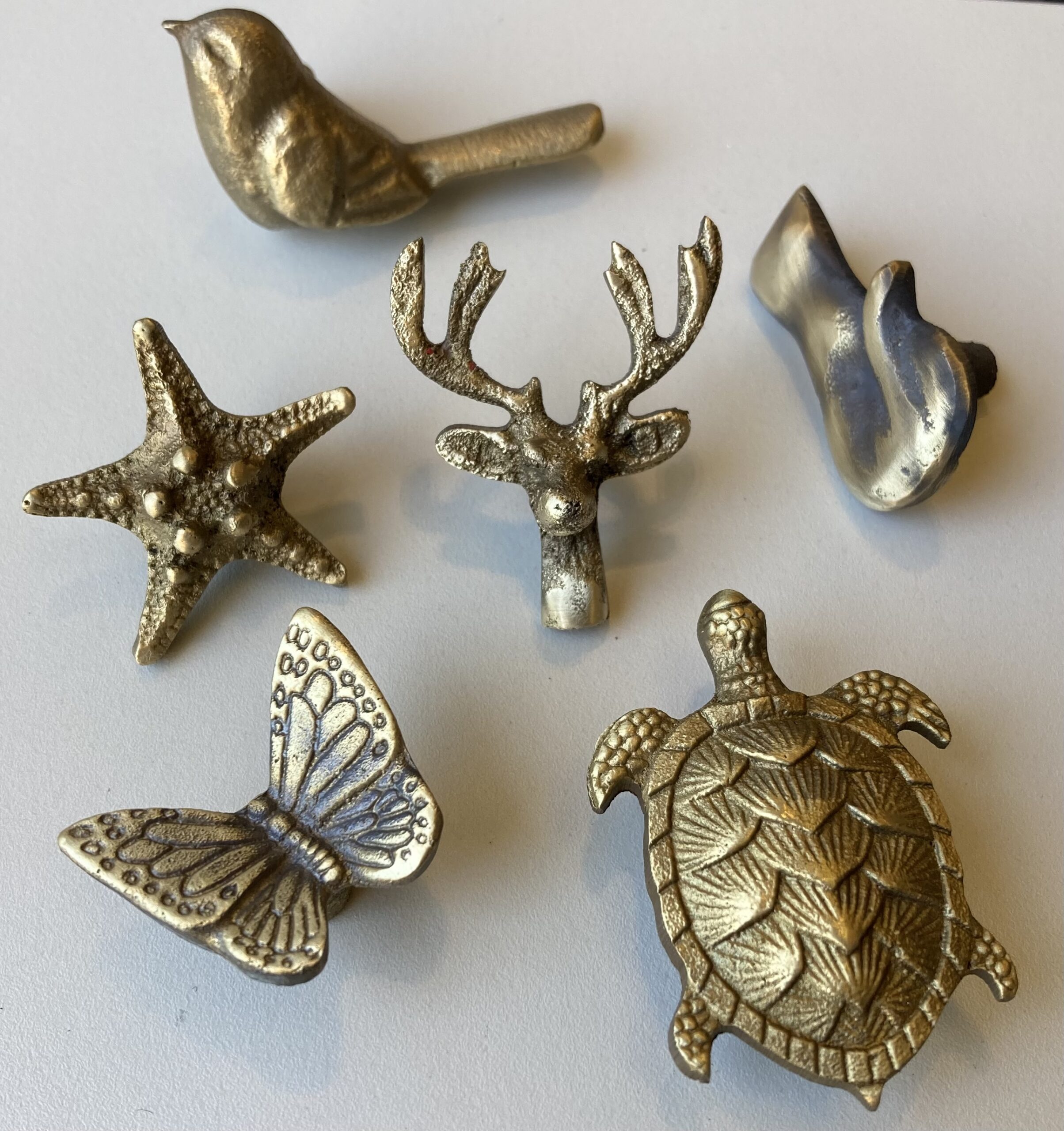 Handmade artisan brass animal cabinet knobs featuring a bird, starfish, deer antlers, butterfly, and highly detailed sea turtle by Stillium.